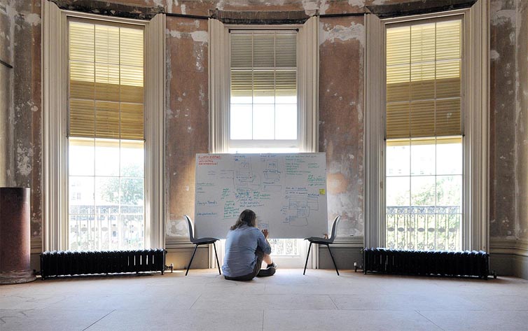 Danny Hope sitting on the floor in front of a whiteboard in an unrestored drawing room.
