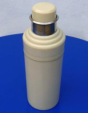 Photograph of cream-coloured cocktail shaker standing on a blue table top.